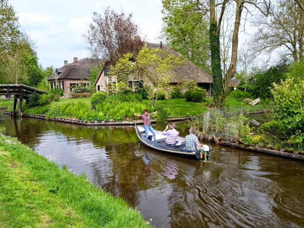 Een open bootje vaart door een Gieterse gracht langs rietgedekte huizen